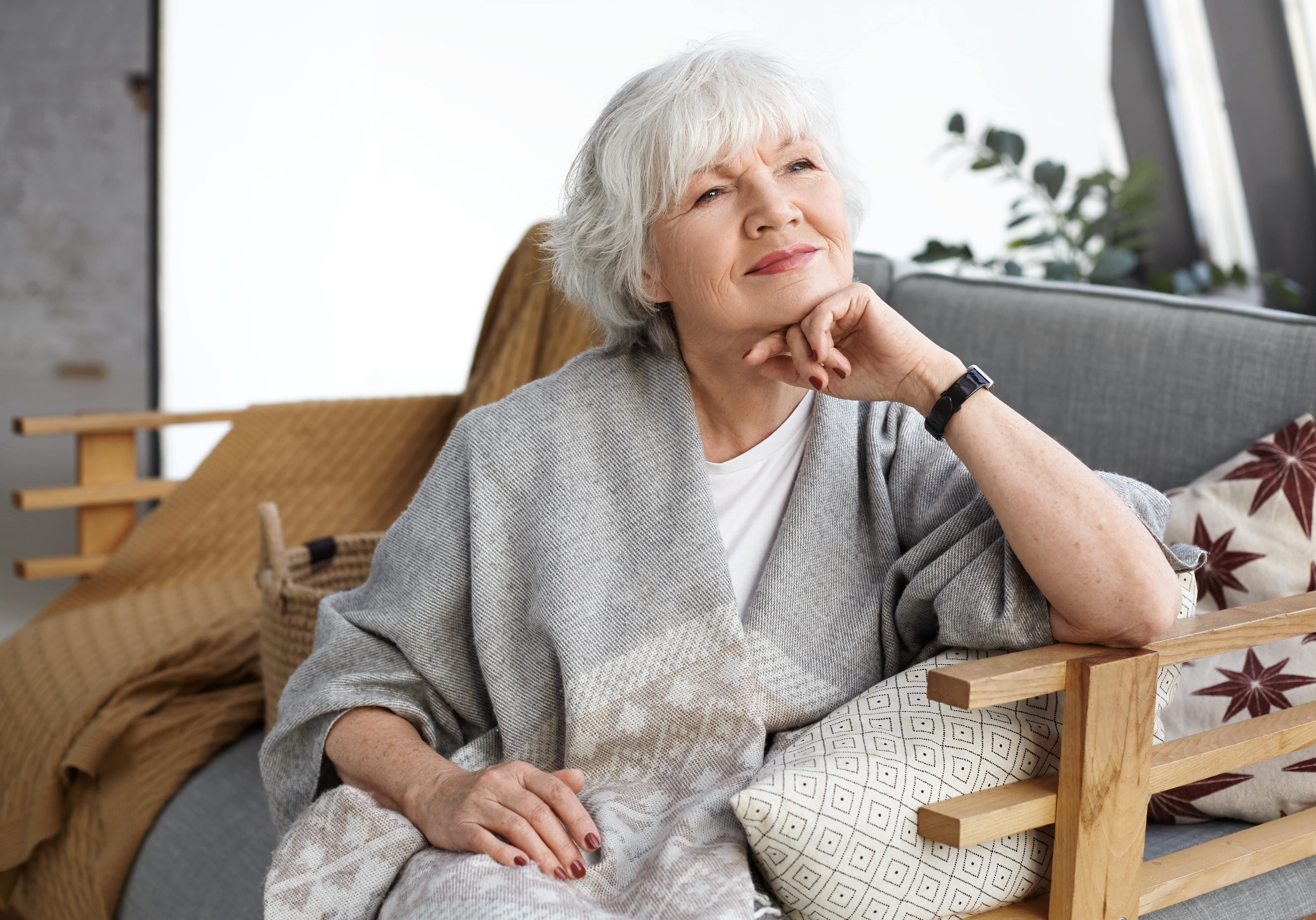 portrait-lovely-middle-aged-grey-haired-european-woman-with-dreamy-smile-eyes-full-wisdom-relaxing-home-alone-sitting-comfortable-couch-reminiscing-about-days-her-youth-min